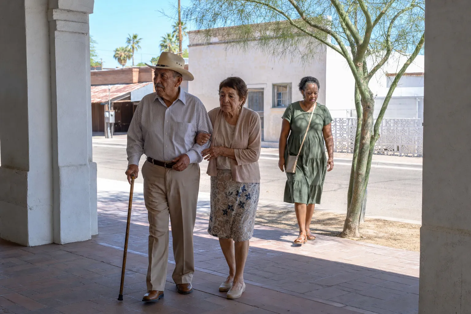 An older man with a cane and a straw hat walking arm in arm with a woman out of the sun into the shade of an arcade.